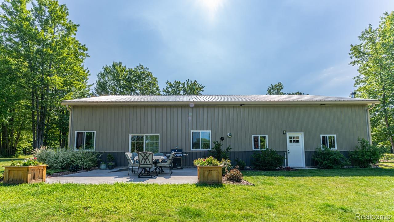 2418 South 41st Road South Cadillac, MI 49601 - Photo 4 of 57 Expansive rear patio area featuring a concrete surface, surrounded by mature greenery and a manicured lawn