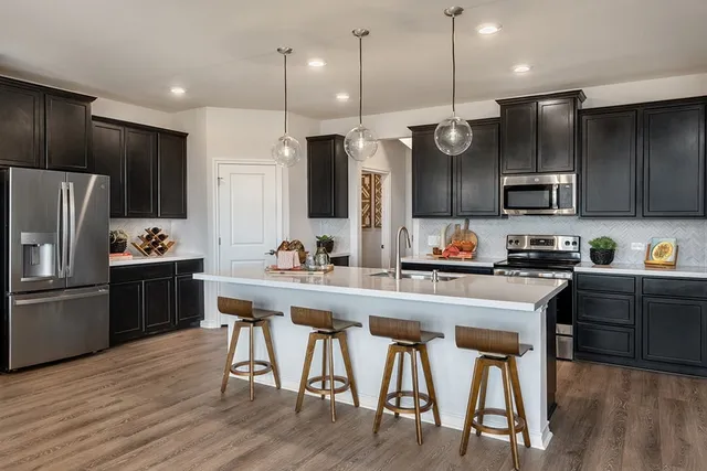 a large kitchen with stainless steel appliances kitchen island granite countertop a sink dishwasher a refrigerator and a dining table with wooden floor