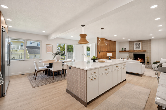 1168 East Center Street Bountiful, UT 84010 - Photo 9 of 38 Open-concept living space featuring a central kitchen island with white cabinetry, wood-finish flooring, recessed lighting, and a prominent fireplace with a light brick surround and wood mantel