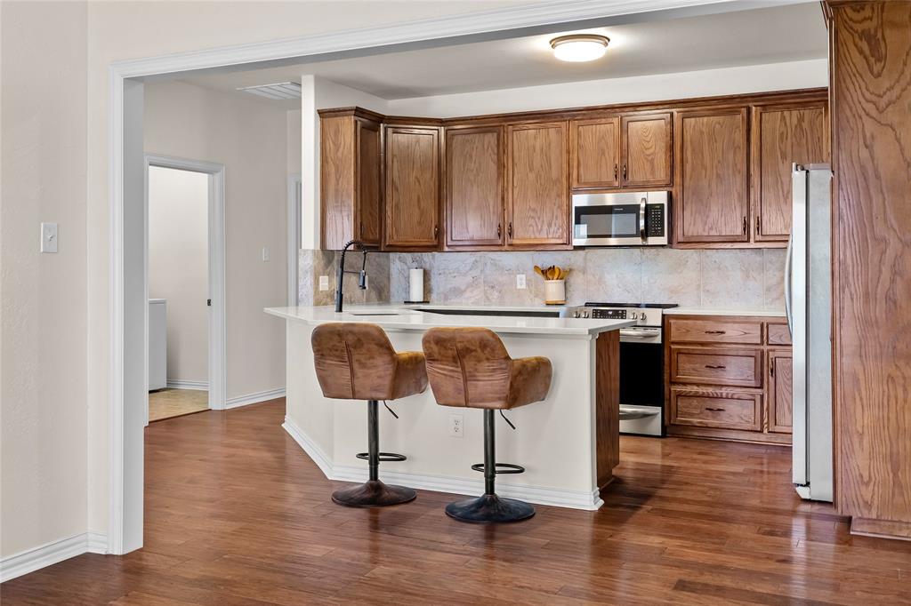 1308 Madeline Street Commerce, TX 75428 - Photo 13 of 37 a kitchen with stainless steel appliances granite countertop a stove top oven a sink dishwasher a dining table and chairs with wooden floor