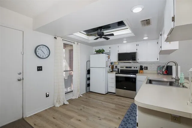 a kitchen with stainless steel appliances a stove a sink dishwasher a refrigerator and white cabinets with wooden floor