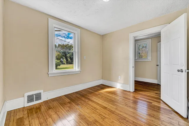 a view of an empty room with wooden floor and a window