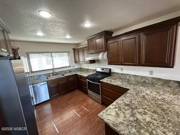 a kitchen with stainless steel appliances granite countertop a refrigerator a sink dishwasher a stove and white countertops with wooden floor
