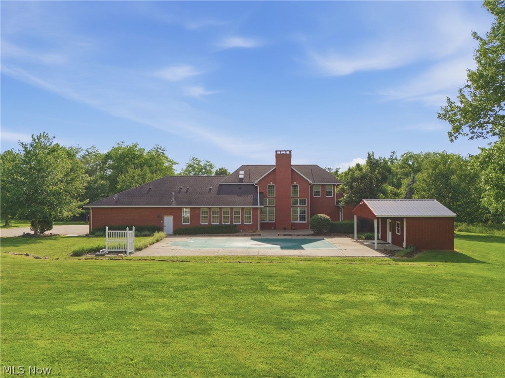2184 Brenner Road Northeast Carrollton, OH 44615 - Photo 44 of 50 Expansive rear grounds featuring a red brick residence with multiple windows, a swimming pool with surrounding patio, a detached shed with an overhang, and a lush green lawn
