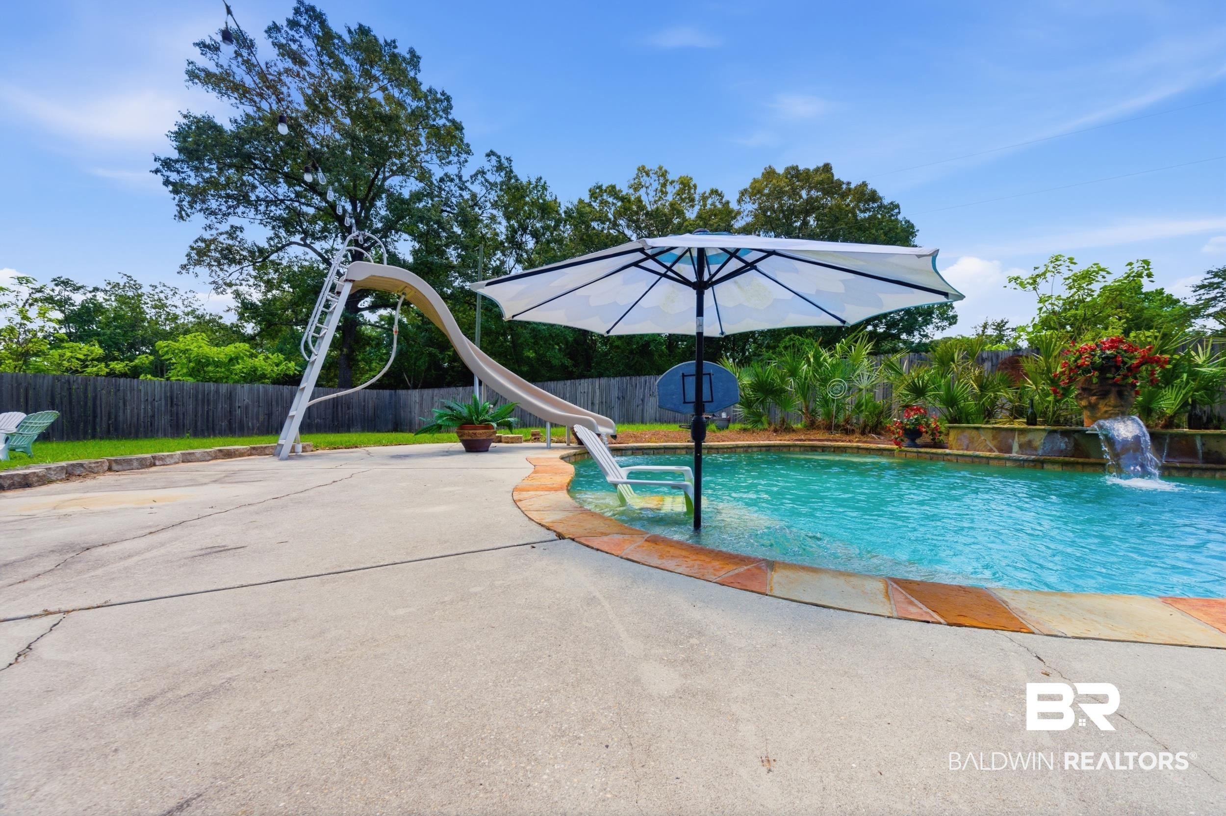 51620 Robert White Road Bay Minette, AL 36507 - Photo 72 of 81 Concrete pool deck surrounding a kidney-shaped swimming pool with a stone coping and a waterfall feature