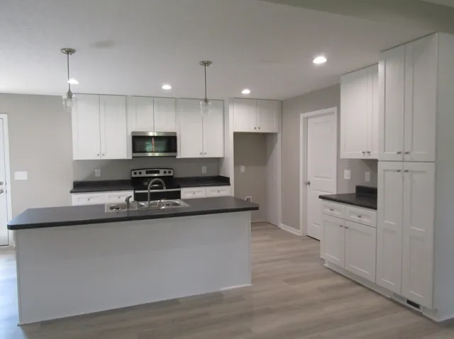 a kitchen with stainless steel appliances a refrigerator stove a sink and white cabinets