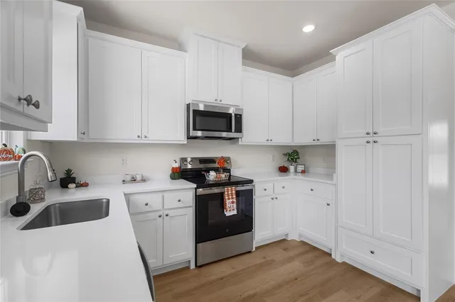 a kitchen with stainless steel appliances granite countertop white cabinets a sink a stove a refrigerator and microwave with wooden floor