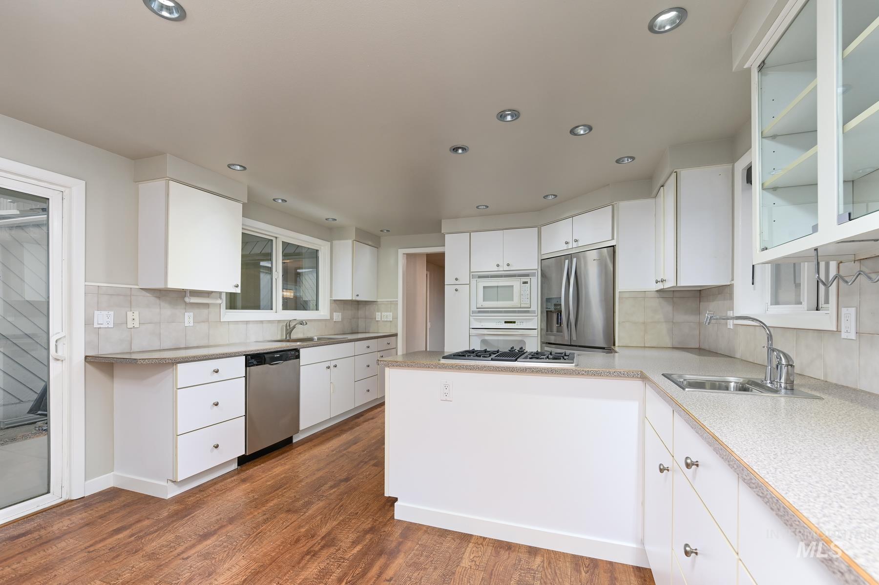 7208 West Cascade Street Boise, ID 83704 - Photo 5 of 49 Kitchen featuring white cabinets, stainless steel appliances, dark wood-style floors, a peninsula, and backsplash