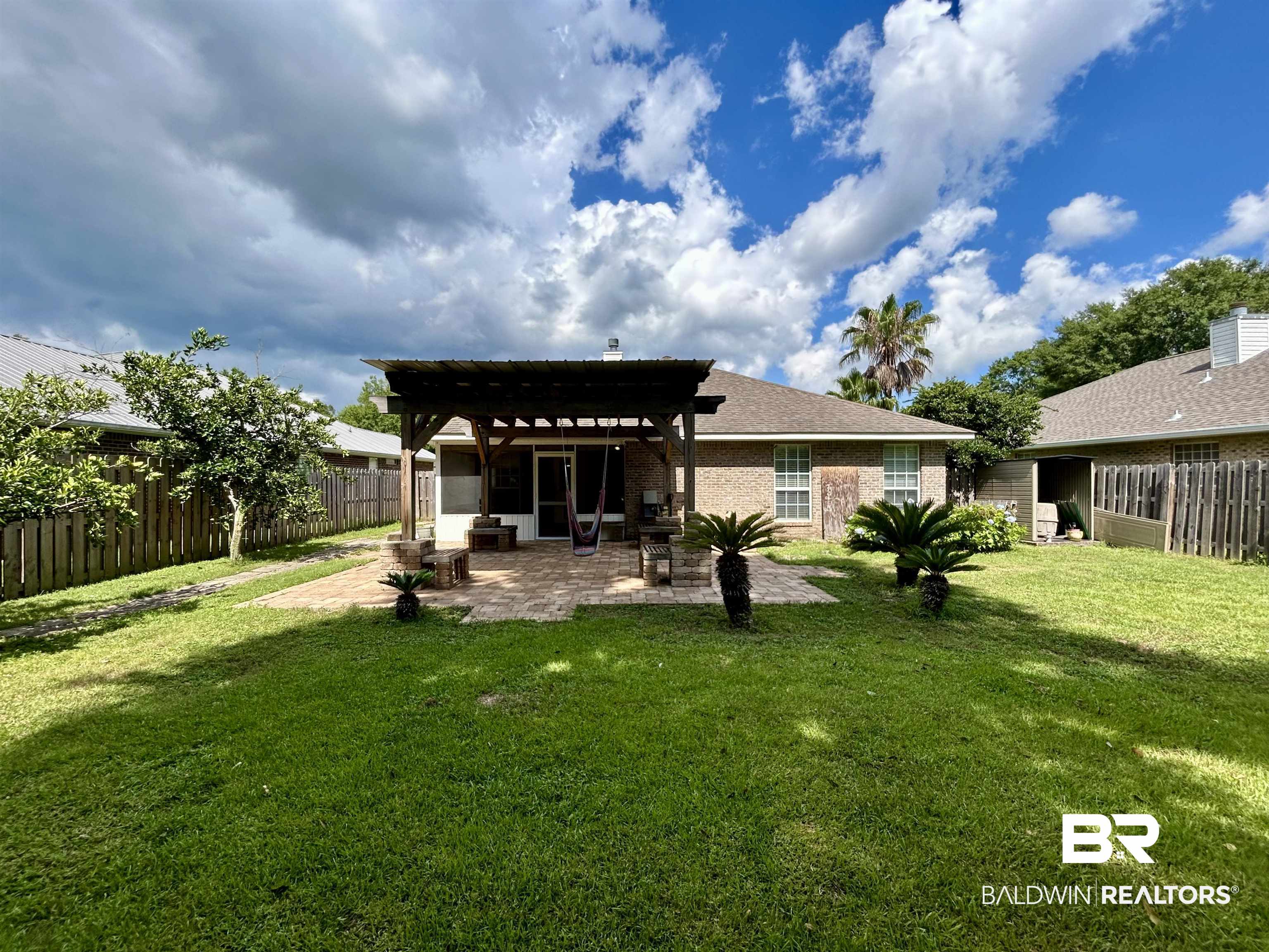 7198 Raintree Lane Gulf Shores, AL 36542 - Photo 31 of 33 Spacious backyard featuring an extensive paver patio, an attached pergola structure, and a screened-in porch with an exterior door