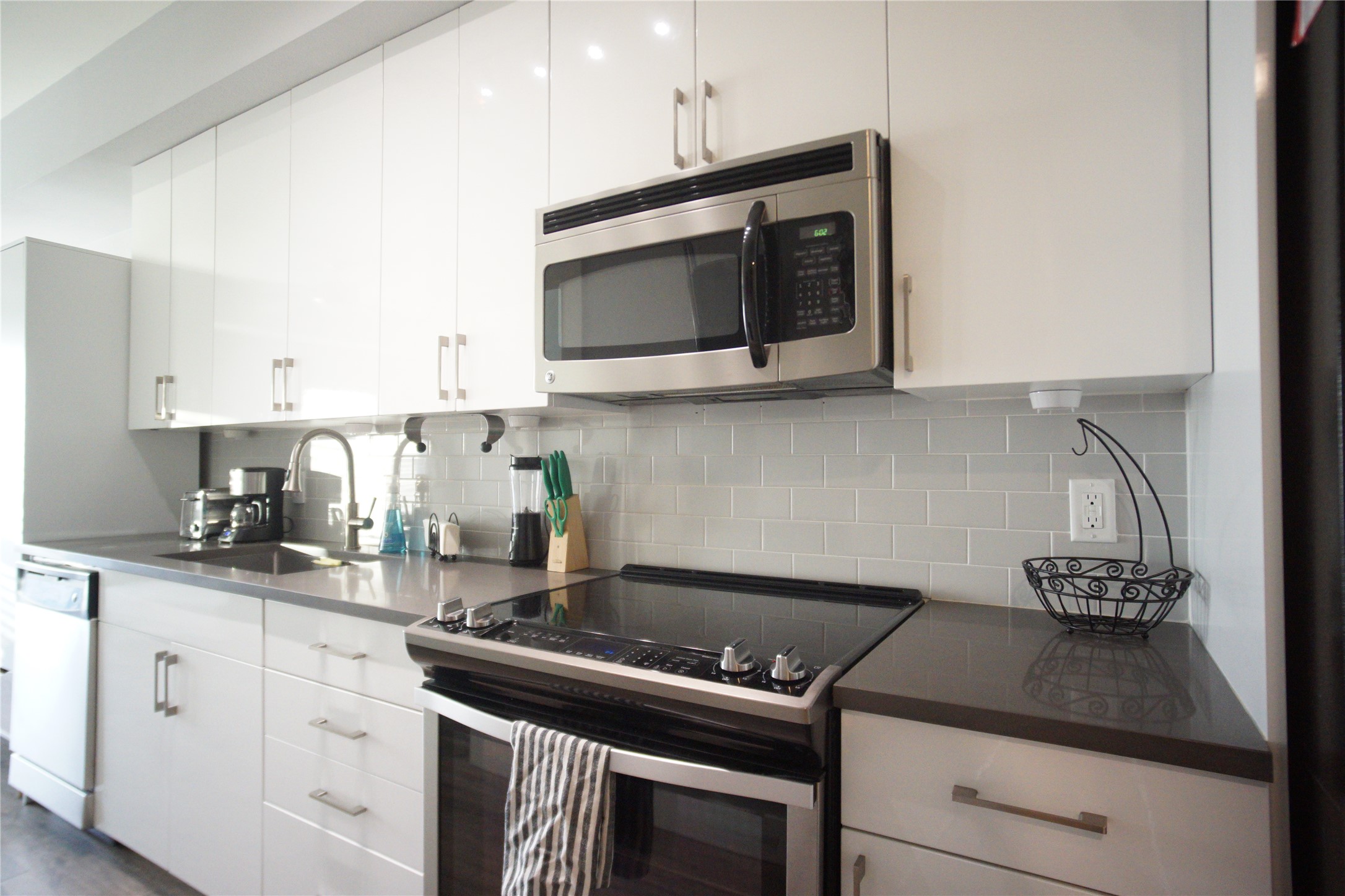 Modern galley kitchen with sleek cabinetry, stone countertops, stainless steel appliances, and subway tile backsplash.