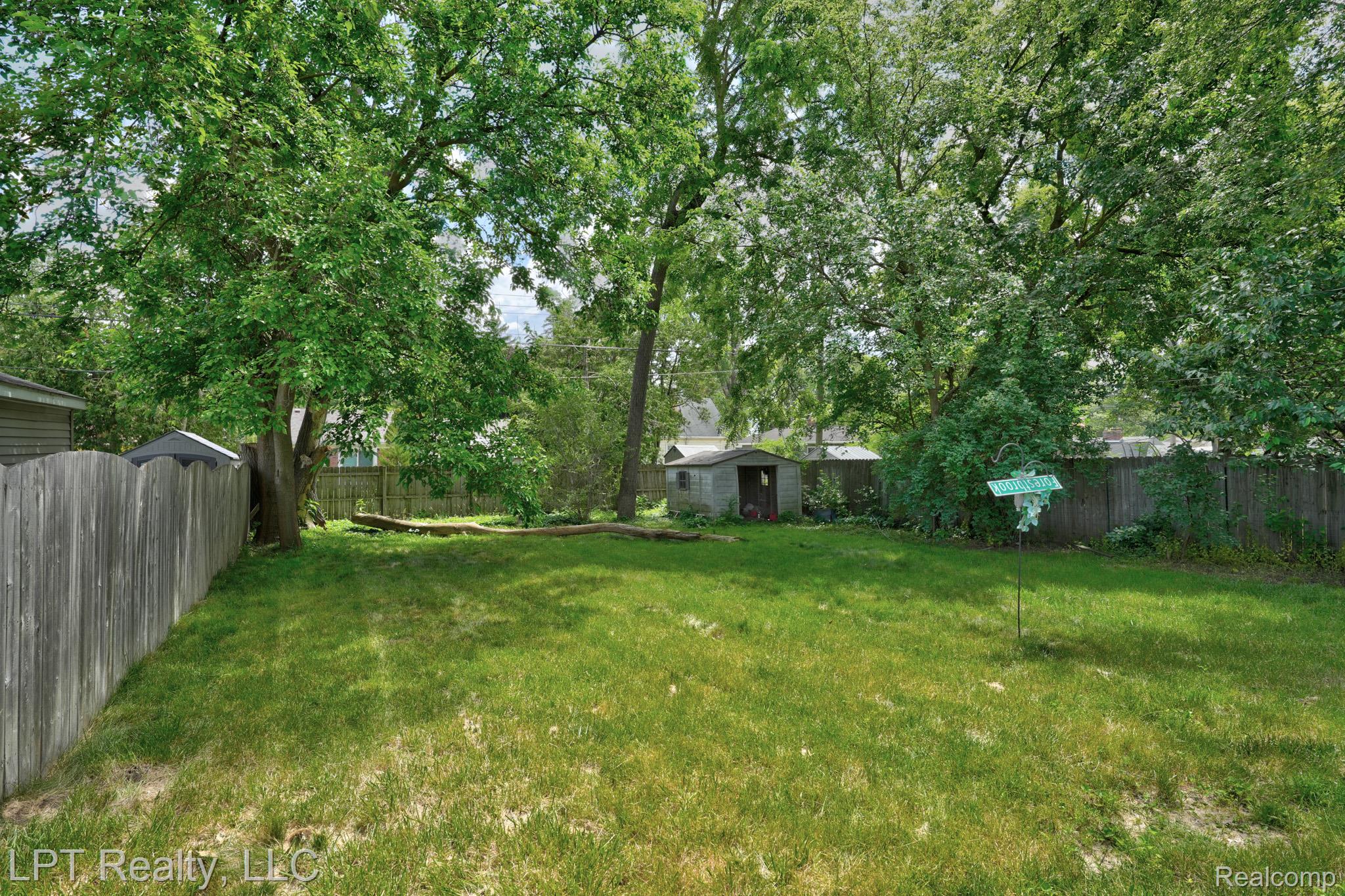 23038 Violet Street Farmington, MI 48336 - Photo 28 of 29 Expansive backyard featuring mature trees, a wooden privacy fence, a storage shed, and a lush lawn