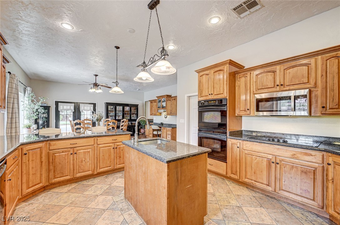 1140 Mahoney Avenue Logandale, NV 89021 - Photo 2 of 51 Kitchen with dark stone counters, a textured ceiling, a center island with sink, pendant lighting, and black appliances