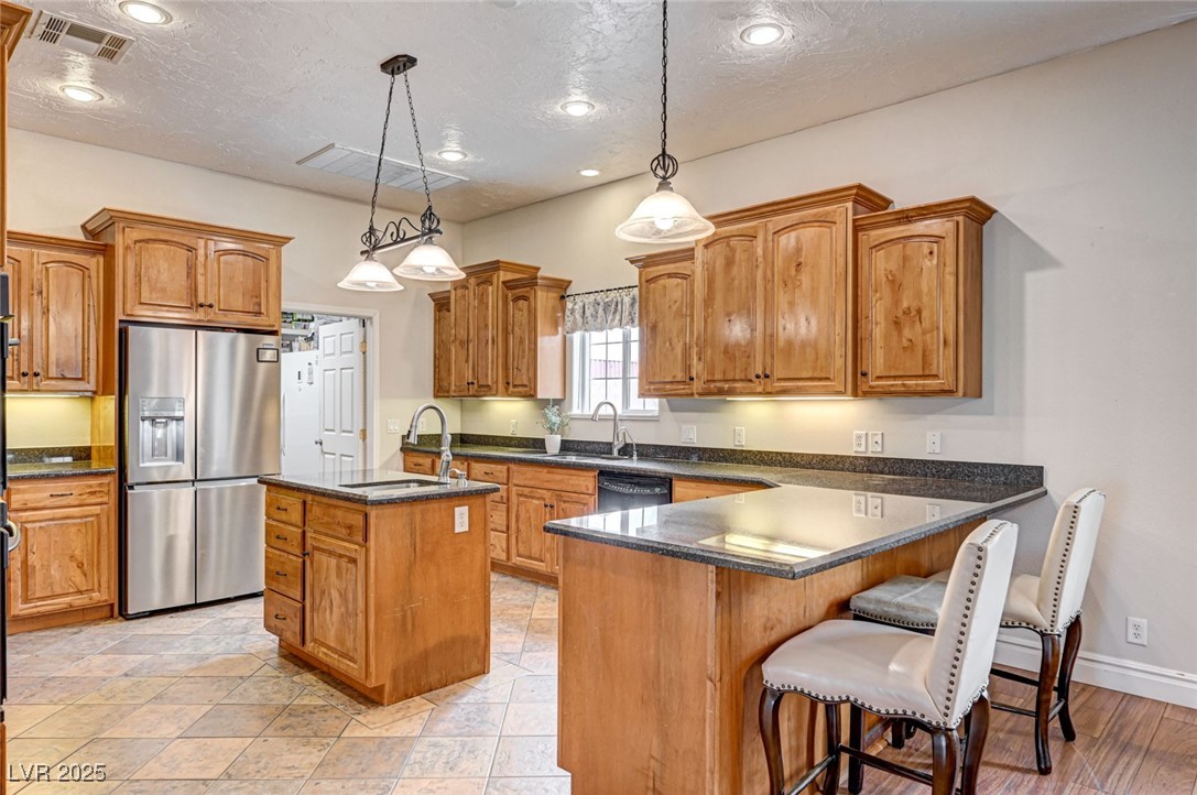 1140 Mahoney Avenue Logandale, NV 89021 - Photo 22 of 51 Kitchen featuring a center island with sink, stainless steel refrigerator with ice dispenser, pendant lighting, dark stone counters, and a textured ceiling