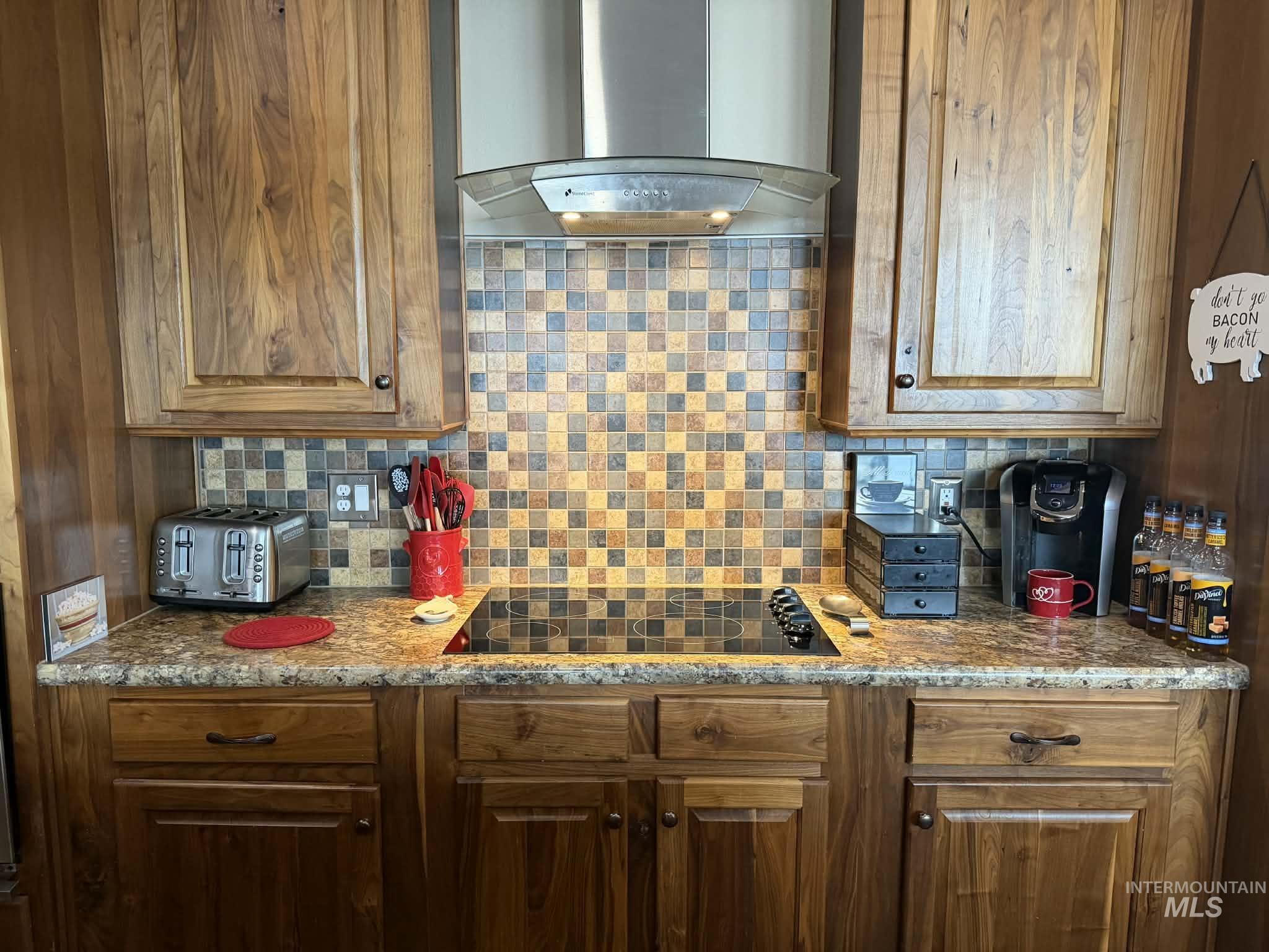 19378 Homestead Loop Lewiston, ID 83501 - Photo 31 of 42 Kitchen with wall chimney exhaust hood, tasteful backsplash, black electric cooktop, and brown cabinets