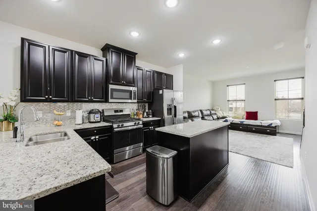 a kitchen with kitchen island granite countertop wooden cabinets a sink dishwasher stove and refrigerator with wooden floor