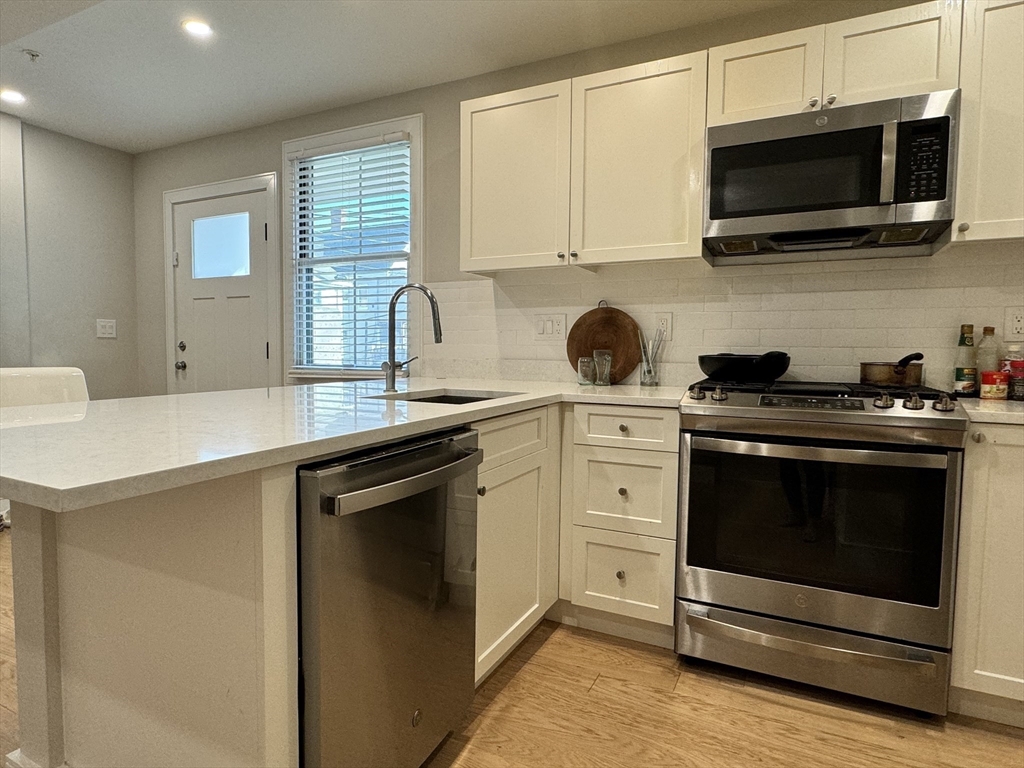 13 Greylock Road, Unit 1 Boston, MA 02134 - Photo 4 of 11 a kitchen with stainless steel appliances granite countertop grey cabinets a stove a sink and dishwasher next to a window