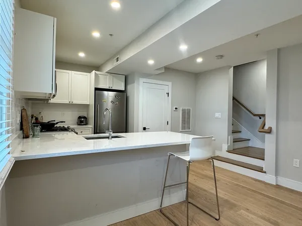 a large kitchen with stainless steel appliances kitchen island a stove a refrigerator a sink dishwasher a stove and white cabinets with wooden floor