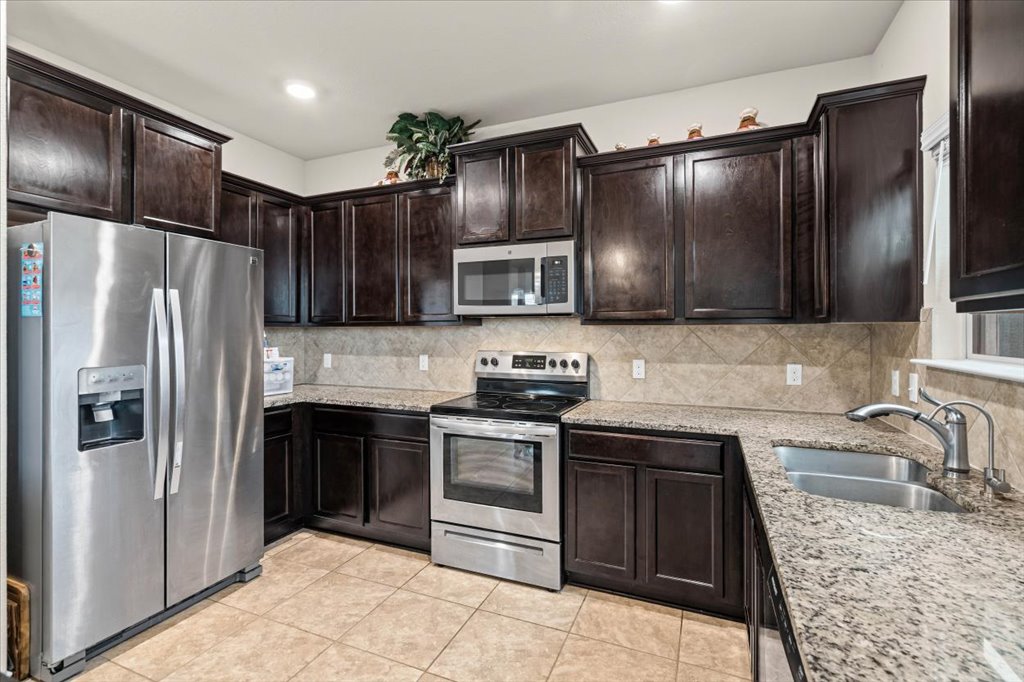 212 Plata Lane Jarrell, TX 76537 - Photo 11 of 30 Kitchen featuring stainless steel appliances, light stone counters, dark wood finish cabinetry, decorative backsplash, and light tile patterned flooring