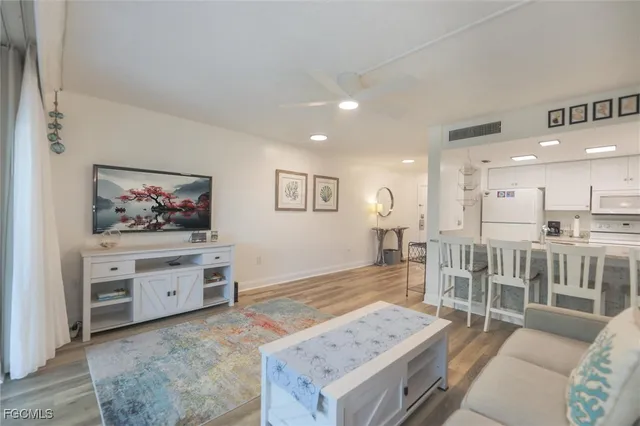 a living room with stainless steel appliances kitchen island granite countertop a stove a sink a dining table and chairs with wooden floor