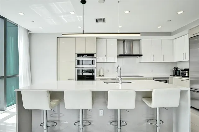 a kitchen with stainless steel appliances a sink a stove a refrigerator cabinets and a dining table