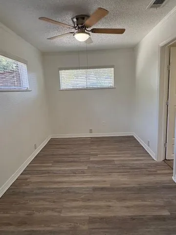 a view of an empty room with wooden floor ceiling fan