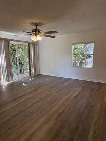 an empty room with wooden floor chandelier fan and windows