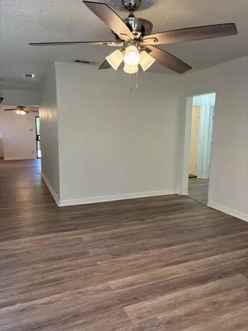 a view of an empty room with wooden floor and a ceiling fan
