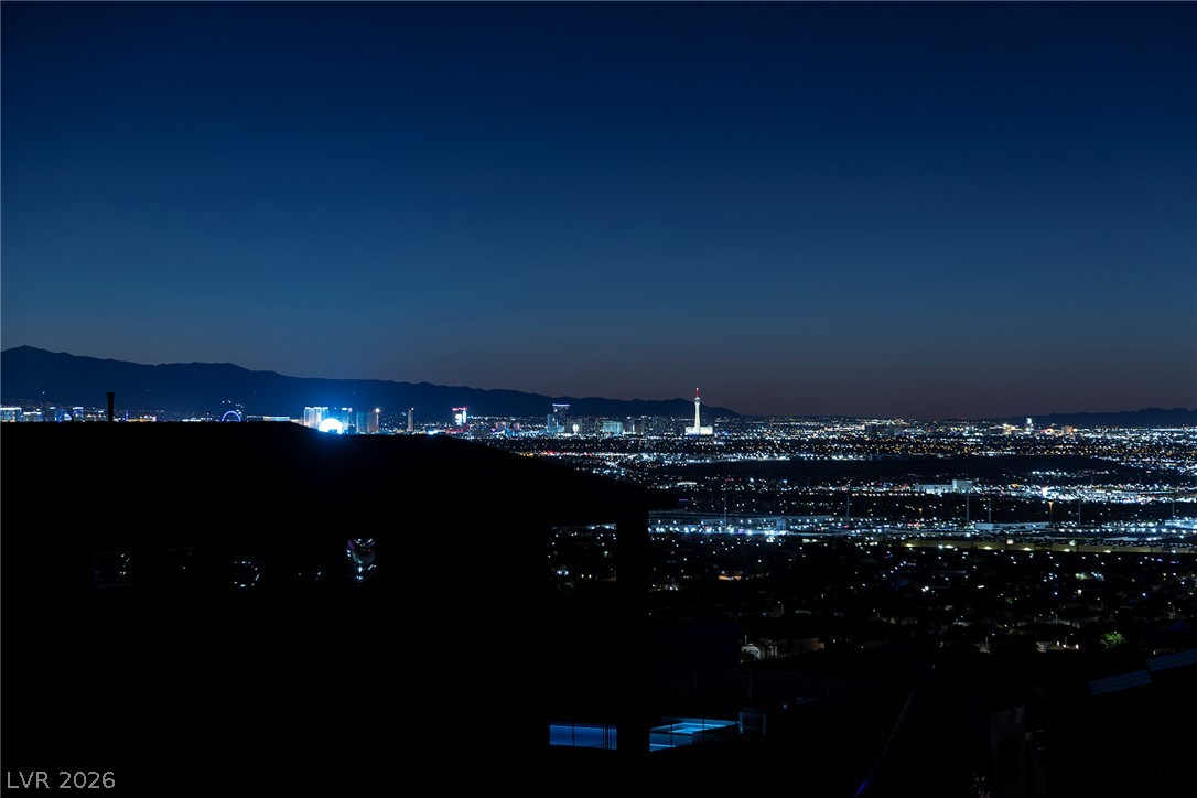 526 Riley Ridge Henderson, NV 89012 - Photo 7 of 10 City lights sparkle against the mountain backdrop, revealing a vibrant cityscape under a twilight sky.