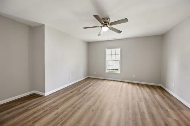 an empty room with wooden floor fan and windows