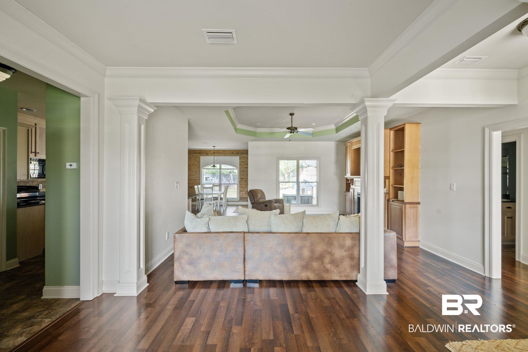 3879 Symphony Way West Semmes, AL 36575 - Photo 8 of 34 Living room with ceiling fan, a raised ceiling, decorative columns, and dark wood-type flooring