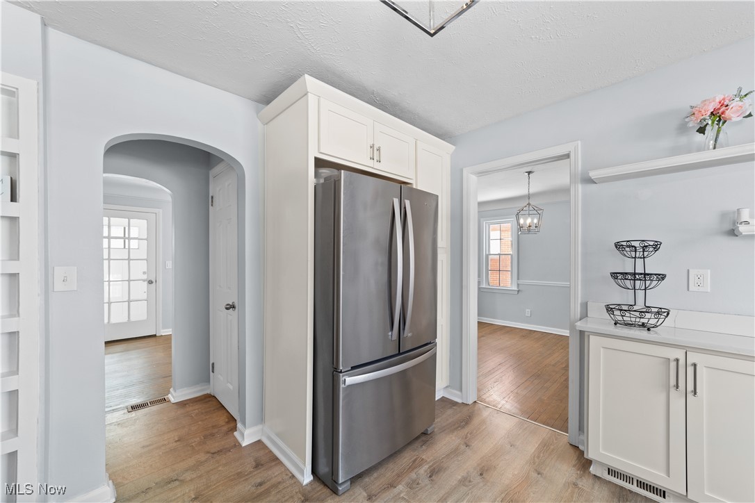 4249 Stonehaven Road Cleveland, OH 44121 - Photo 12 of 33 Kitchen with a textured ceiling, white cabinets, pendant lighting, stainless steel refrigerator, and light wood-type flooring
