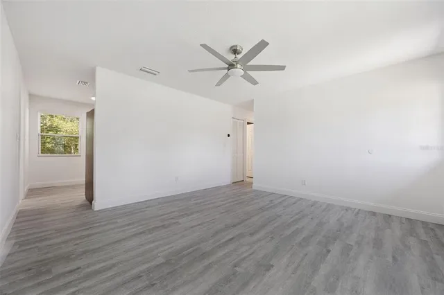 an empty room with wooden floor window and ceiling fan