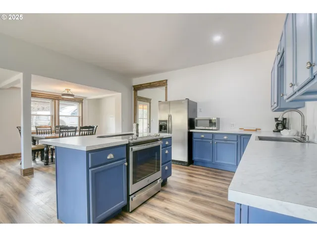 a kitchen with stainless steel appliances kitchen island granite countertop a stove top oven a sink dishwasher a dining table and chairs with wooden floor