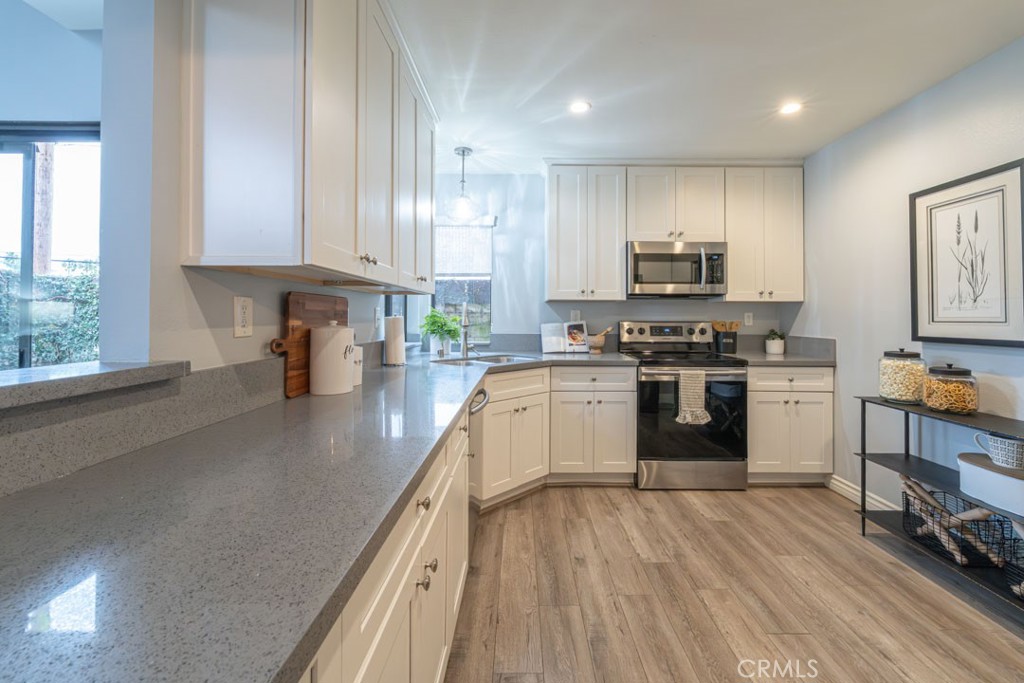 5002 East Atherton Street Long Beach, CA 90815 - Photo 11 of 52 a kitchen with stainless steel appliances white cabinets a sink dishwasher a stove and a refrigerator with wooden floor