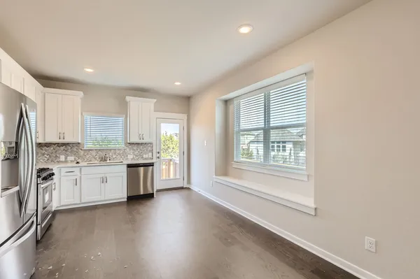 a kitchen with stainless steel appliances granite countertop a stove a sink dishwasher a refrigerator and white cabinets with wooden floor