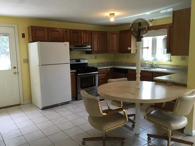 a kitchen with stainless steel appliances granite countertop a refrigerator a sink a stove a dining table and chairs