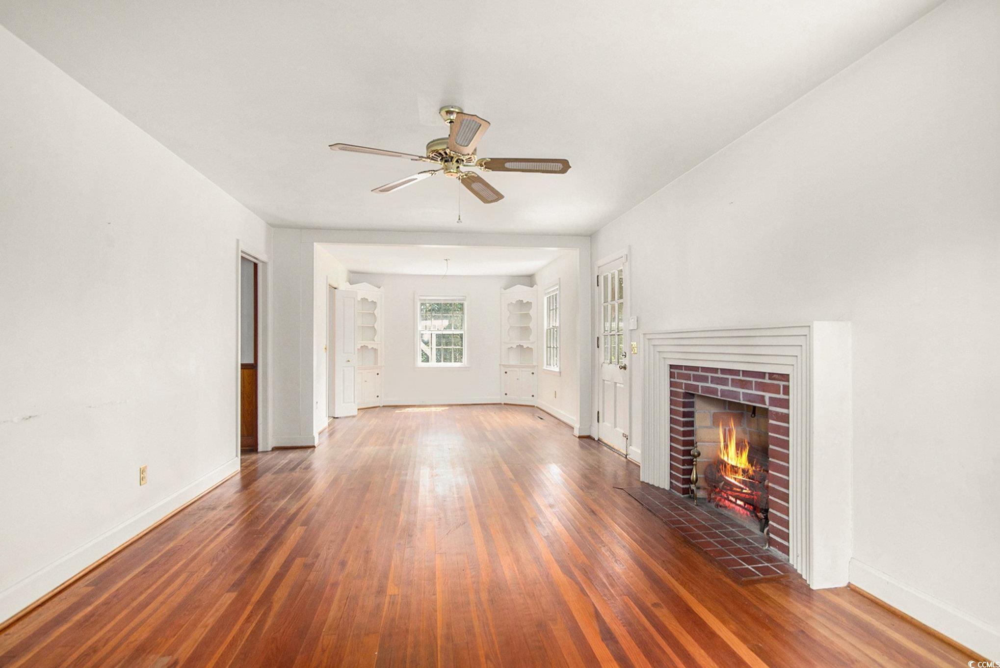 1008 North Main Street Marion, SC 29571 - Photo 5 of 27 Unfurnished living room featuring dark wood-type flooring, a brick fireplace, and a ceiling fan