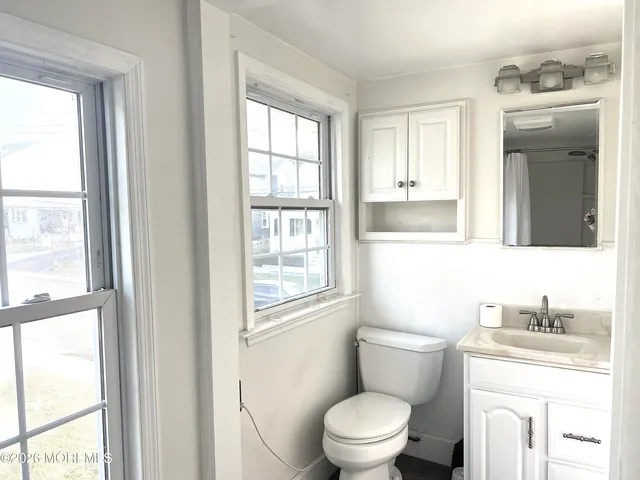 a bathroom with a granite countertop toilet a sink a mirror and next to a window