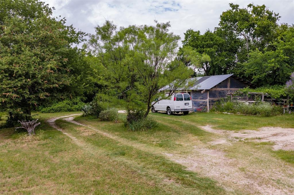1007 West Belt Line Road Cedar Hill, TX 75104 - Photo 25 of 30 Gravel driveway leading to a metal-roofed outbuilding with fencing, surrounded by mature trees and natural landscaping