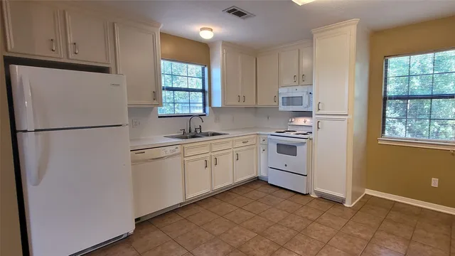 an empty room with chandelier fan and kitchen view