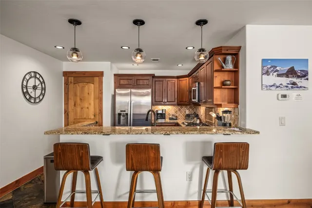 a kitchen with stainless steel appliances granite countertop a dining table chairs and a refrigerator