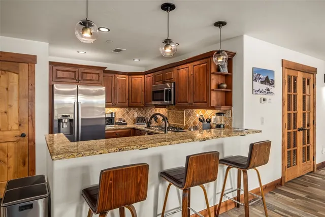 a kitchen with stainless steel appliances granite countertop a refrigerator a sink dishwasher a stove a dining table and chairs with wooden floor