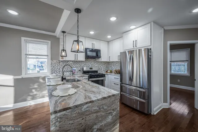 a kitchen with stainless steel appliances granite countertop a refrigerator a sink dishwasher a stove and white cabinets with wooden floor