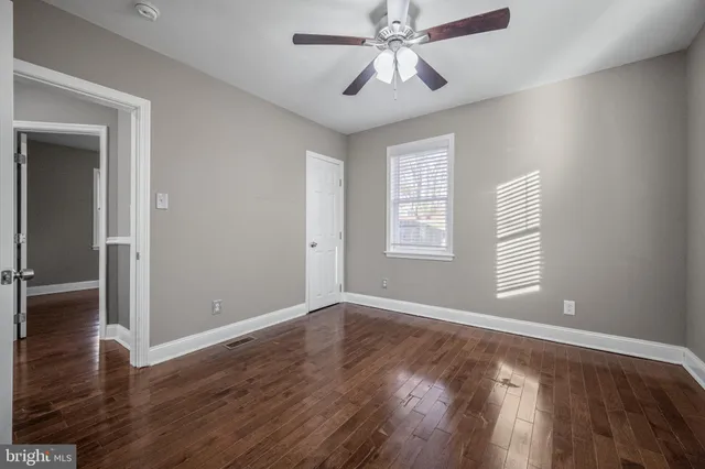 an empty room with wooden floor chandelier fan and windows