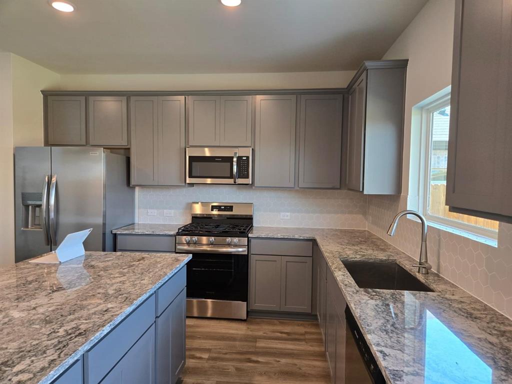 508 Weller Road McKinney, TX 75069 - Photo 4 of 16 Contemporary kitchen featuring an island, light gray cabinetry, stainless steel appliances, speckled countertops, and a hexagonal tile backsplash
