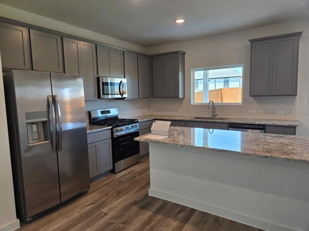 508 Weller Road McKinney, TX 75069 - Photo 5 of 16 Modern kitchen featuring stainless steel appliances, grey cabinetry, granite countertops, and wood-finish flooring