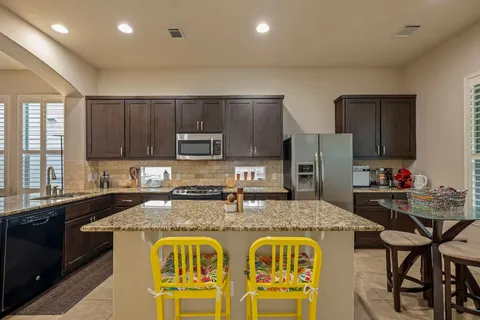 a kitchen with stainless steel appliances granite countertop a stove top oven a sink a refrigerator and chairs