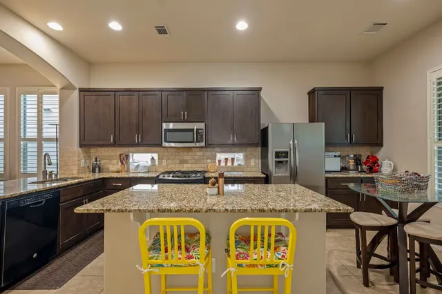 a kitchen with stainless steel appliances granite countertop a stove top oven a sink a refrigerator and chairs
