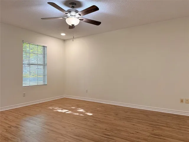 an empty room with wooden floor chandelier fan and windows