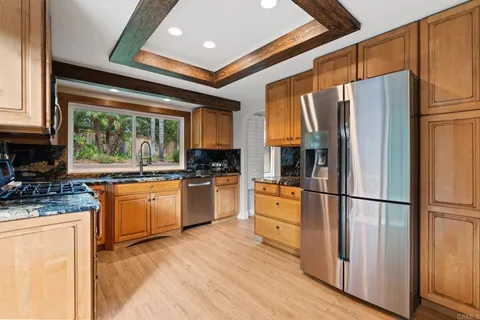 a kitchen with stainless steel appliances granite countertop a refrigerator a sink dishwasher a stove and white cabinets with wooden floor